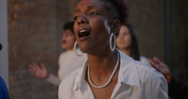 Huzurlu bir ifadeyle şarkı söyleyen bir kadın, bir kilise ayini sırasında ruhaniliğe ve inanca dalmış, arka planda aydınlatılmış bir haç