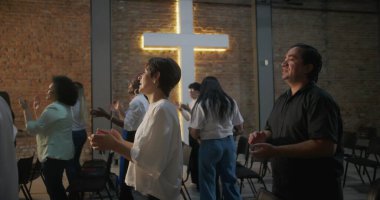 İçten ibadete katılan bireyler ellerini kaldırmış, arka planda haç aydınlatmış, kilise ayini sırasında sadakat, birlik ve inanç ifadeleri sergiliyorlar.