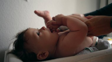 Bebek masasını değiştiriyor, anne kucağında bebek bezi, çocuk hafifçe gülümsüyor, rutin bakım, her gün ebeveyn ile etkileşim, rahatlık ve bakım, yakın ilişki..