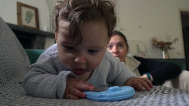 Bebek koltuğa yaslanırken mavi nesneyle oynuyor, anne arkadan izliyor, bebek keşfe çıkıyor, eğlenceli bir öğrenme anı, evde anne ile vakit geçiriyor..