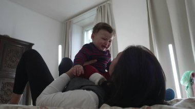 Anne yatakta ağlayan bir bebek tutuyor, duygusal bir anda rahatlatıyor ve sakinleştiriyor, sakin bir ev ortamında çocuk bakımını ve erken çocukluk gelişimini gösteriyor..