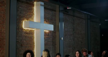 İbadet eden bir grup insan kilisenin içinde büyük aydınlatılmış haç yakınında toplandı. Barışçıl ve huzurlu bir ortamda birlik, inanç ve ruhsal bağlantıyı yansıtıyorlar.