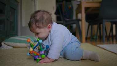 Bebek yerde oturuyor, neşeli bir oyuncakla oynarken neşeyle gülüyor, neşeli ve eğlenceli bir keşifle meşgul, sıcak bir ev ortamında eğlenceli aile vakitlerinin tadını çıkarıyor.