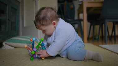 Bebek yerde oturuyor, neşeli bir oyuncakla oynarken neşeyle gülüyor, neşeli ve eğlenceli bir keşifle meşgul, sıcak bir ev ortamında eğlenceli aile vakitlerinin tadını çıkarıyor..