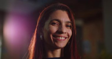 Genç Latin kadın hafifçe dışarıda gülümsüyor. Yumuşak bir ışık, rahat ve doğal bir ifade. Omuzlarından uzun kızıl saçlar akıyor.