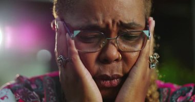 Afrikalı Amerikalı kadın gözlerini kapatıyor ve duygusal bir anda yüzünü ellere bastırıyor. Üzüntü, üzüntü ya da zihinsel yorgunluk belirtileri gösteriyor.