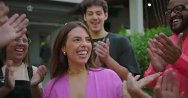 Dışarıda toplanan arkadaşlar tarafından alkışlanırken merkezde dikilmiş gülen genç bir kadın, kutlama ve kişisel başarılarından dolayı takdir edilen neşeli bir an.