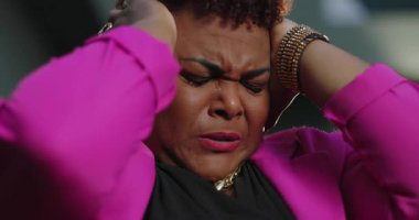 Afro-Amerikalı bir kadın başı dertteyken gözleri sıkıca kapalı pembe ceket ve altın takılar takıyor hayal kırıklığını ve zihinsel bunalımı ifade ediyor.