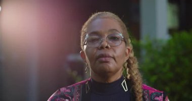 Kendinden emin Afrikalı Amerikalı kadın, sakin bir ifadeyle kameraya bakıyor, bahçe ortamında dikiliyor, bilgelik, itibar ve sessizlik saçıyor.