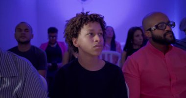 Genç çocuk kilise ayini sırasında dikkatle oturur. Etrafı cemaatle çevrili, odaklanmış ve düşünceli bir şekilde.