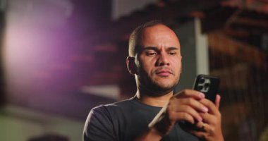 Latin kökenli, Afrika kökenli, akıllı telefona gülümseyen, açık havada eğlenen, ekranda görülen komik bir şeye gerçek bir eğlenceyle tepki veren bir adam.