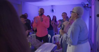 Vaiz, kilise ayininin neşeli kapanış anına liderlik ediyor. Cemaat gülümsüyor, alkışlıyor ve ruhani birlik içinde şarkı söylüyor.