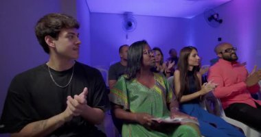 Cemaat kilise toplantısı sırasında sevinçle alkışlıyor, farklı geçmişlere sahip insanlar sırayla oturup mesajlara ruhani birlik ve bağlılıkla cevap veriyorlar.