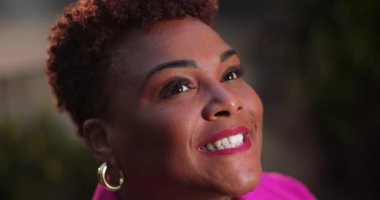 Afrika kökenli Amerikalı bir kadın gökyüzüne doğru gülümsüyor. İnancını, umudunu ve duygusal sıcaklığını açık havada, yumuşak doğal ışıkta ifade ediyor.