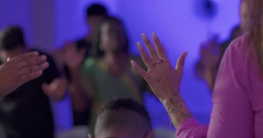 İbadet sırasında elini kaldıran İspanyol kadının eli, arka planda bulanık ibadet edenler ve kolektif ibadet sırasında ellerini kaldıranlar.