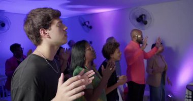 Kilisedeki çeşitli cemaatler elleri havada ve gözleri kapalı ibadet eder. İnsanlar coşkulu bir övgü oturumunda inançla birleşir.