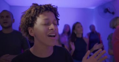 Genç çocuk kilisenin ibadet ayini sırasında sevinçle şarkı söylüyor, manevi birlik içinde kutlama yapan cemaatle çevrili ve övgülerle dolu.