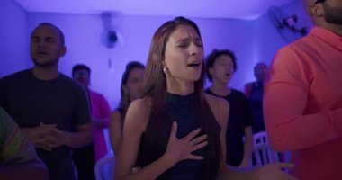 Genç kadın ellerini göğsüne koyuyor ve dua ederken kapalı gözlerle şarkı söylüyor. Etrafı ruhani odaklarla çevrili.