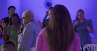 Afrikalı Amerikalı vaiz, İspanyol ve Latinlerle çevrili, gözleri kapalı ve elleri ruhsal birlik içinde dua eden Protestan ayinine liderlik ediyor.