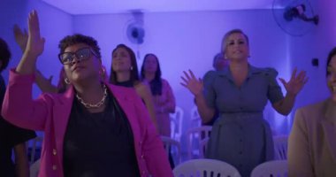 Evanjelik kilise ayini sırasında çeşitli ibadet grupları arasında neşeli ifadeler ve dinsel enerjiyle küçük bir odada şarkı söyleyen ve alkışlayan cemaat.