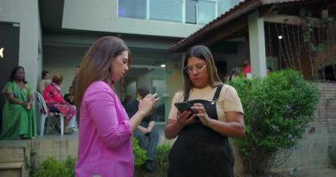 Açık hava buluşması sırasında konuşan ve elinde akıllı telefonlar tutan iki kadın. Bir tanesi telefonundaki içeriği dostça açıklarken bir şey anlatıyor.