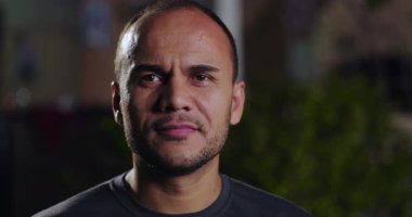 Latin Latin bir adamın yakın plan portresi. Ciddi bir ifadeyle geceleyin açık havada duruyor. Arka plan bulanık ve odaklanmış yüz hatlarıyla.