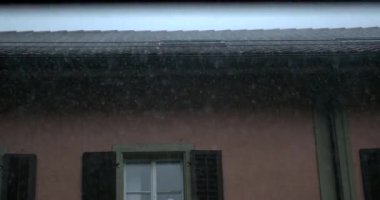 Bardaktan boşanırcasına yağan yağmur, koyu renk kepenkleri ve görünür damlacıkları olan pembe konut binasının döşeli ve kapalı pencerelerine yağar.