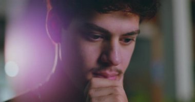 Derin düşüncelere sahip Latin kökenli genç bir adam, elleri çenesinde, dalgın bir ifadeyle aşağıya bakıyor, renkli bokeh 'li yumuşak bir şehir geçmişi var.