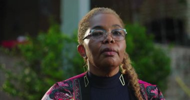 Olgun Afro-Amerikalı kadın kameraya ciddi bir ifadeyle bakıyor. Doğal ortamının dışında duruyor. Sakin ve sakin.