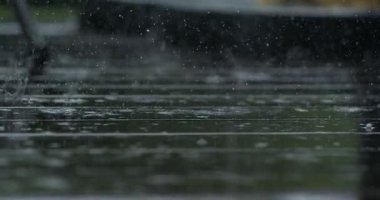 Yoğun yağış sırasında ağır yağmur damlaları ağır çekimde koyu ahşap güverte yüzeyine sıçrıyor. Su dalgalanmaları ve damlacıkları dramatik bir şekilde yakınlaşıyor.