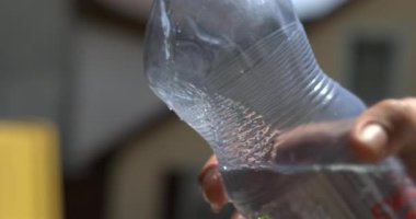 Güneşli bir günde yüksek hızlı kamerayla süper yavaş çekimde çekilen, içi su dolu temiz plastik şişeyle dolu el ele tutuşmuş.