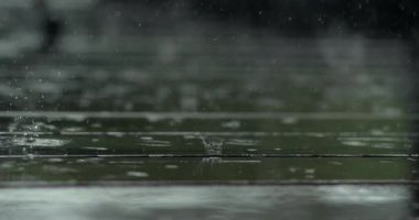 Yağmur, ahşap güvertenin üzerine ağır çekimde düşer. Görünür damlacıklar yüksek detaylarda zıplar ve dağılır. Bulanık arka plan çarpıcı bir atmosfer etkisi yaratır.