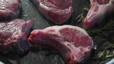 Biberiye üzerine yerleştirilmiş yağlı tavadaki çiğ kuzu pirzolasının üst görüntüsü, mermer dokusuyla görülebilir ve ısıya hazır.