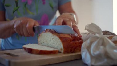 Yumuşak somun ekmeği tahta tahtada bıçakla dilimleyen eller, kabuklu yüzey ve evcil mutfakta görülen kabarık doku..