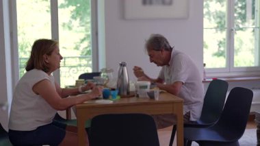 Üst düzey bir çift, yemek masasında birlikte kahvaltı yapıyor. Yoğurt, kahve ve meyveli sabah yemeğinin keyfini çıkarıyorlar.