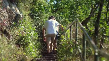 Yaşlı çift yaz yürüyüşü sırasında sık bitki örtüsü, ağaçlar ve korkuluklarla çevrili kırsal taş basamaklarda tırmanıyor.