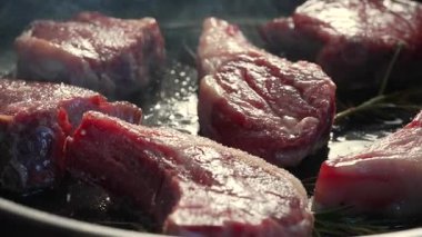 Baharatlı kuzu pirzolası tavada görünür mermer ve yağdan önce ızgara, ortam ışığı ham dokuyu ve yüzey kontrastını yakalıyor.