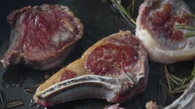 Tavada kısmen pişmiş kuzu pirzolası, kurutulmuş üstler ve görülebilir yağ, biberiye ve yağla çevrili, kırsal alanda sulu mermer eti gösteriyor.