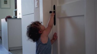 Bebek çabayla kapı tokmağına uzanıyor, modern evdeki kapıyı açmaya çalışıyor, parmak uçlarında gelişigüzel duruyor.