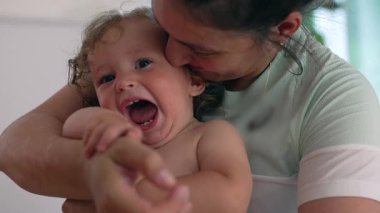 Anne gülümsemeyi kucağında tutarken nazikçe göğsünü gıdıklıyor, hem gülümsüyor hem de yanak yanağa bastırıyor sıcak, samimi bir yakınlık anında.