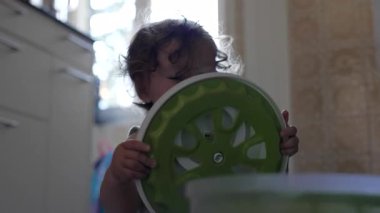 Bebek, mutfak zemininde oturmuş ev eşyalarıyla uğraşırken salata fırıldağı kapağında el sıkışıyor.