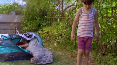 Evin bahçesinin yakınındaki çimlerin üzerinde battaniye ve oyuncaklarla çevrili küçük bir çocuk şapkasıyla arka bahçede aniden ortaya çıkan çadırın yanına adım atıyor..