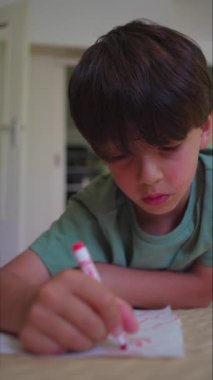 Yerde yatarken kırmızı kalemle çizen odaklanmış çocuk, yoğun bakışlar ve titremeyen eller huzurlu odada beyaz çarşaflarda çizgiler oluşturuyor.