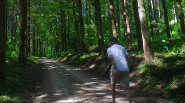 Yaşlı adam orman yolunda tek başına yürüyor. Etrafı uzun ağaçlarla çevrili. Huzurlu bir öğleden sonra ormanlık alanda yalnızlık ve hareketlilik anı.