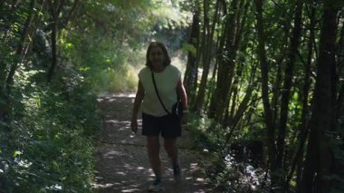 Yaşlı kadın orman yolunda yürüyor, destek için el ele yokuş yukarı yürüyor, yaz boyunca ağaçlar ve yeşil bitkilerle çevrili.
