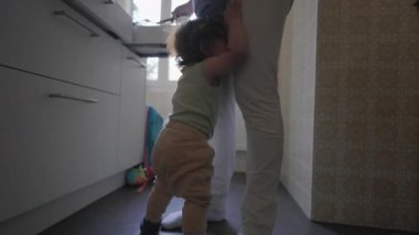 Yeni yürümeye başlayan bir çocuk mutfakta kollarını kaldırmış ve şikayet ifadesini takınarak ebeveyn telefonun yanında dururken alınmak istiyor.