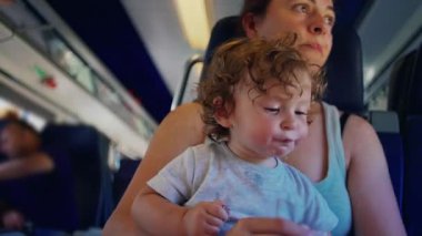 Anne, dinlenme anında hem odaklanmış hem de sessiz bir şekilde trende otururken bebeğin objeyi incelemesine yardım ediyor.