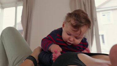 Bebek anne göğsünde yatıyor, ayaklara merakla bakıyor, erken keşif, duyusal gelişme, bağlanma, öğrenme, ebeveyn-çocuk bağı, sıcaklık, sevgi, güven.