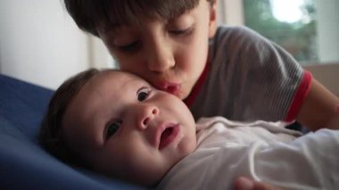 Kardeş bebek yanağına yoğun bir öpücük, sevgi dolu ama ezici kardeş etkileşimi, çocukluk yakınlığı, koruyucu kucaklama, aile sevgisi, duygusal bağ.