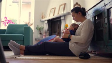 Anne bebekle yerde oturuyor, erken oyunları destekliyor, keşfetmeye teşvik ediyor, ebeveynlik yapıyor, sıcak ve sevgi dolu bir ev ortamı, güvenli çocukluk anları..